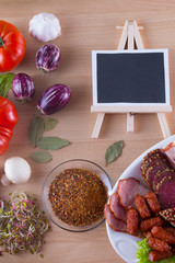 Meat appetizer on plate like jamon, bacon, salami with vegetables and copy space on blackboard.