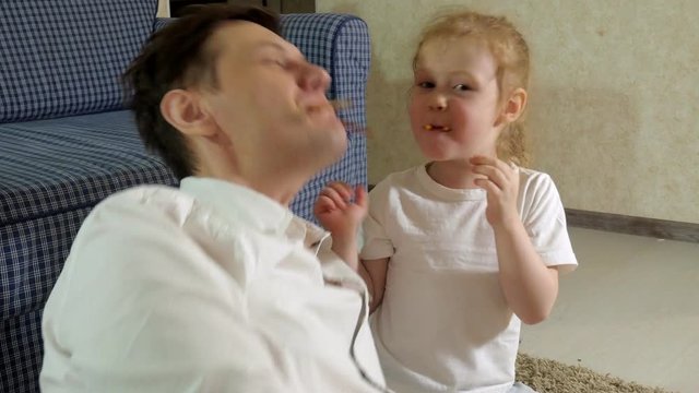 man and daughter watching television, sitting on the floor eating snacks