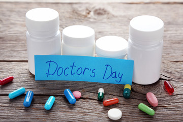 Inscription Doctors Day with pills and bottles on wooden table