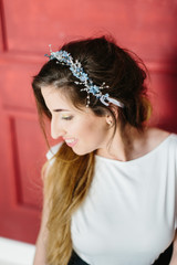 Young beautiful bride with a beautiful diadem in the hair poses sitting on the chair on red background.