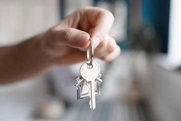 Men hand holding key with house shaped keychain. Modern light lobby interior. Mortgage concept. Real estate, moving home or renting property.