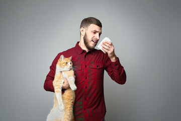 Young man with allergy holding cat on grey background