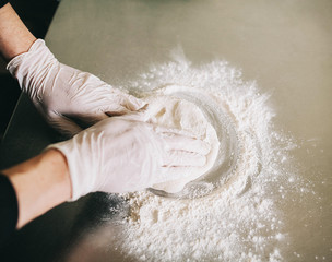 The hands of the men knead the dough on the flour on the kitchen surface - 193348018
