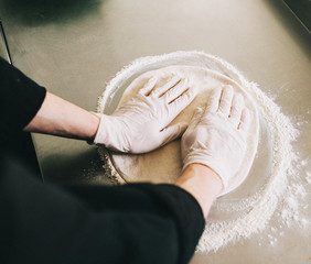 The hands of the men knead the dough on the flour on the kitchen surface - 193348021