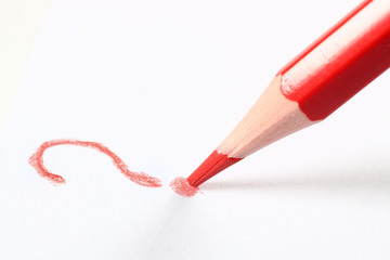 A red pencil writes a white background question mark on a white background