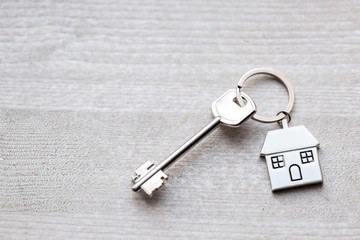 House key and keychain in the form of homes lies on wooden boards. Concept for real estate,...