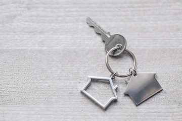 House key and keychain in the form of homes lies on wooden boards. Concept for real estate, mortgage, moving home or renting property.