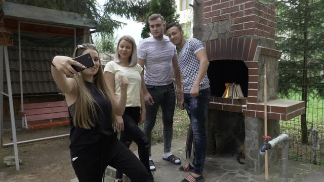 Group of teen friends taking selfies photo using a smartphone in the backyard cooking barbecue with grill in the background