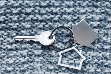 House key and keychain in the form of homes lies on knitted wool fabric. Concept for real estate, mortgage, moving home or renting property.