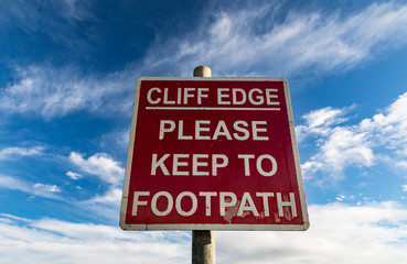 Cuff edge warning sign on footpath trail with sky background