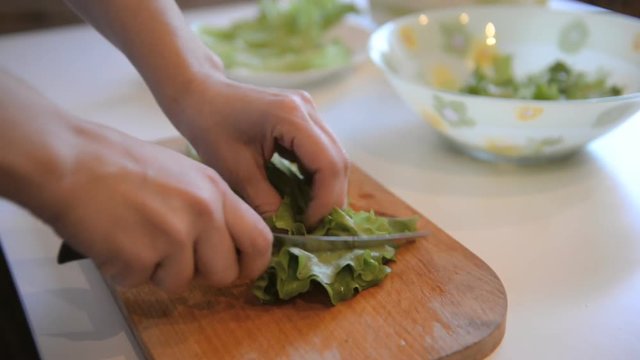 cook cuts salad leaves on a wooden board