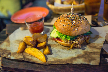 large Burger with potatoes on a wooden stand