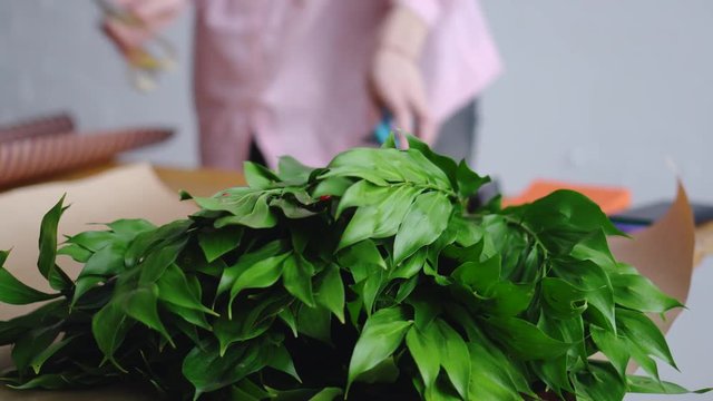 Florist prepares tools to create a beautiful bouquet. Аgainst the background of greenery.