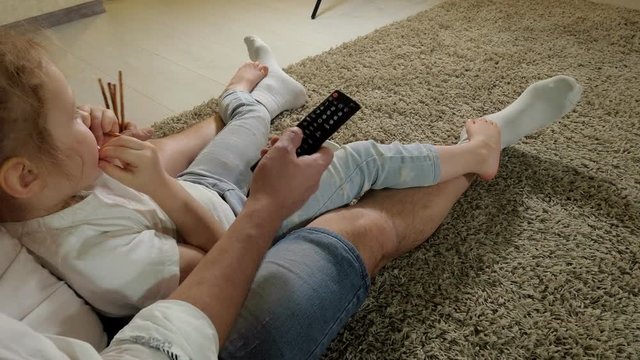 man and daughter watching television, sitting on the floor eating snacks