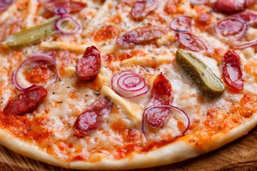 Close up of hot pizza with salami, onions and gherkins served on chopped wood. Food background, restaurant or pizzeria concept