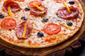 Hot fresh sicilian pizza with bacon, olives and tomatoes served on wood, close up. Italian food, restaurant or pizzeria concept