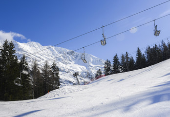 Fototapeta premium Chairlift at Italian ski area on snow covered Alps and pine trees