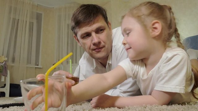 man and daughter watching television, sitting on the floor drink juice