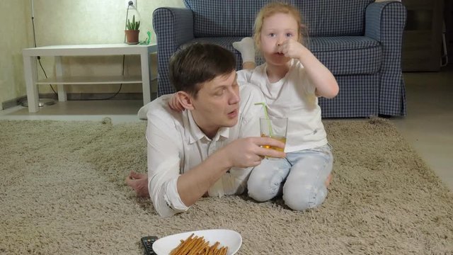 man and daughter watching television, sitting on the floor eating snacks
