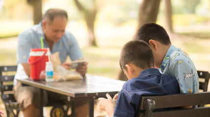 Little boy playing tablet game together in the park while father no attention to kid
