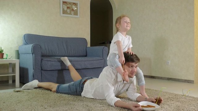 man and daughter watching television, sitting on the floor eating snacks