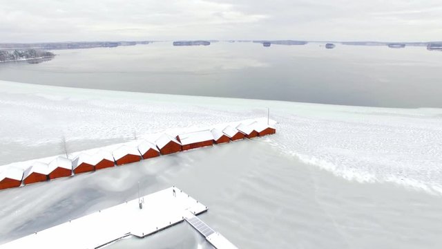 Closing view of row of red boathouses in freezing lake landscape