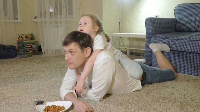 man and daughter watching television, sitting on the floor eating snacks