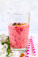 Blueberry smoothies of berries, banana and almonds in glasses with cocktail tubes on a white wooden board.