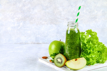 Green smoothies from parsley, salad, kiwi, apple in a bottle on a gray concrete table.