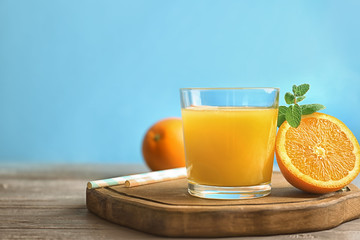 Glass of fresh orange juice with slice on wooden table against color background