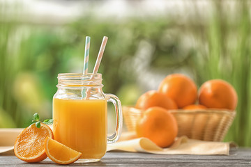 Mason jar of fresh orange juice on wooden table outdoors
