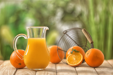 Glass jug of fresh orange juice on wooden table outdoors
