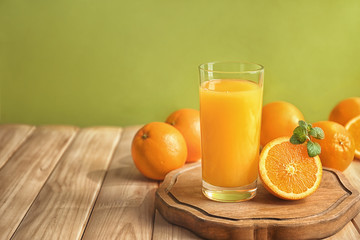 Glass of fresh orange juice with slice on wooden table against color background