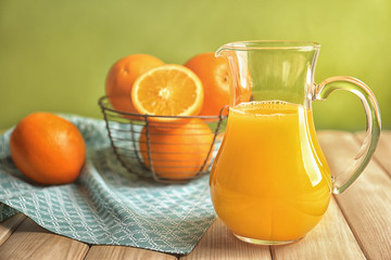 Fototapeta na wymiar Glass jug of fresh orange juice on wooden table against color background