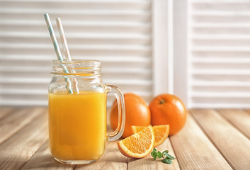 Mason jar of fresh orange juice with slices on wooden table