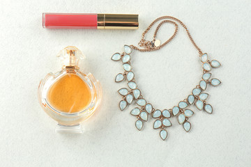 Bottle of perfume, lip gloss and necklace on light background