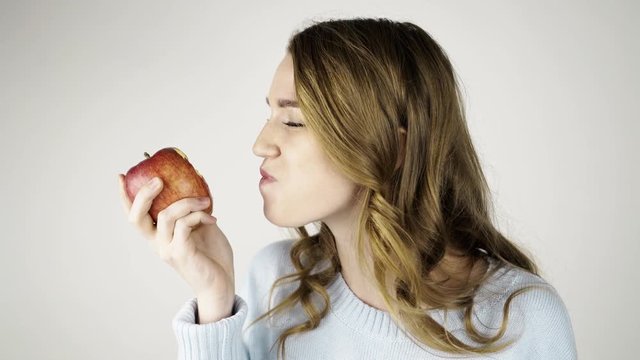 Seductive fair haired woman in gray biting a red juicy apple and chewing it. She is looking at you, licking her lips and flirting. Locked down real time medium shot
