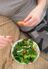 Obraz na płótnie Canvas girl in jeans sits on the sofa and holds a fork and plate with vegetables. Mixed vegetables. Arugula, celery and spinach and carrots. top view. vegan breakfast meal in bowl
