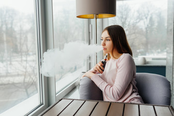 Modern girl smoking vape.Trendy new vaping device,smoke e-liquid instead of nicotine cigarettes.Tobacco free e-juice. Vaping concept
