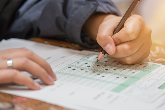 high school or university student hands taking exams, writing examination on paper answer sheet optical form of standardized test on desk doing final exam in classroom. Education  literacy concept.