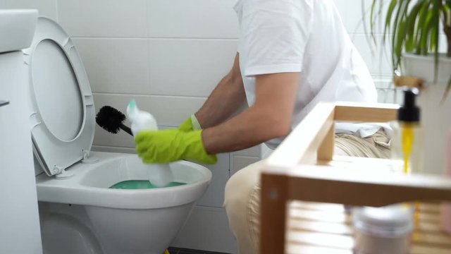 The man at work. Man with a rubber glove cleans a toilet bowl using means for cleaning