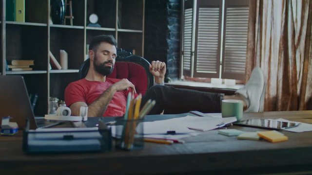 Tired businessman putting feet on table and listening music in headphones in office. Young business man relaxing at workplace. Handsome manager resting after hard working day
