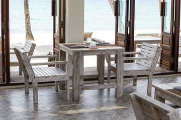 Table and wooden chairs in empty cafe next to the sea water on the beach, Thailand