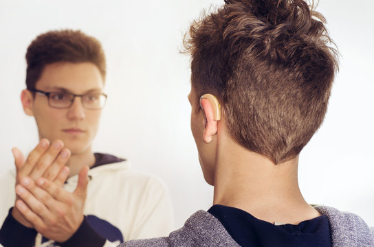 
Deaf mute teenager talking with sign language, back view , focus on hearing aid 
