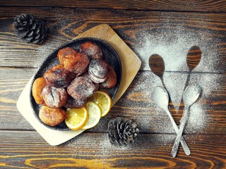  жаренные оладушки на чугунной сковородке с  сахарной пудрой и  шишками на деревянном фоне