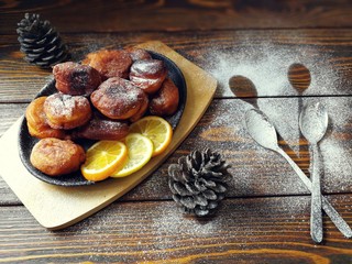  жаренные оладушки на чугунной сковородке с  сахарной пудрой и  шишками на деревянном фоне