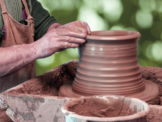 Hands of a Potter make a pot on a pottery wheel on green background.