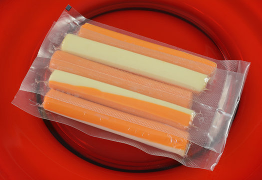 Close up of cheddar and mozzarella cheese mixed sticks in individual portion plastic packaging human or canine snacks on red plate