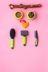 Grooming equipment for pets near bowls with animal feed on pink bakground top view copy space