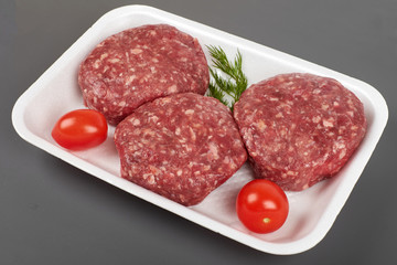 Tray with raw beef burgers isolated on gray background